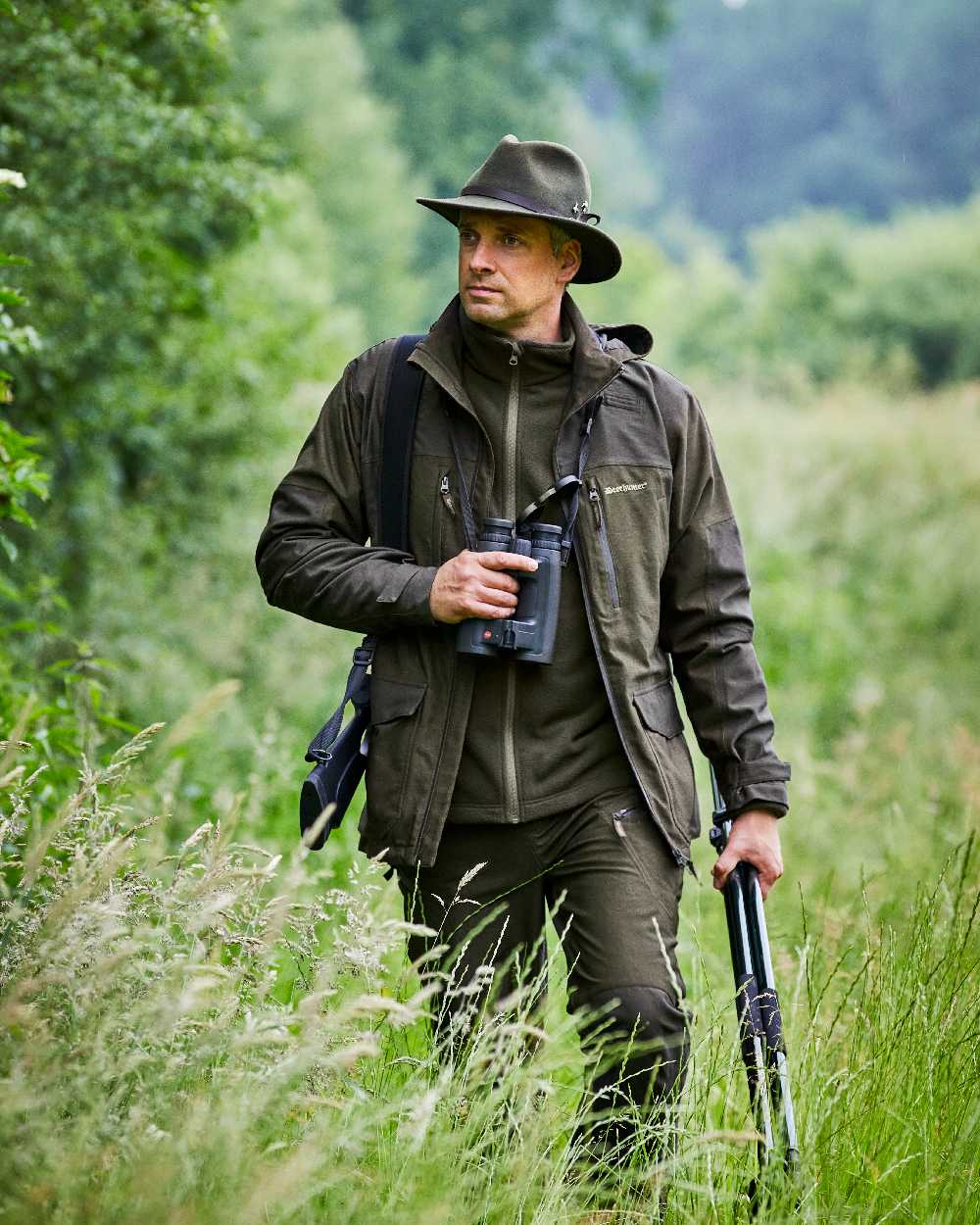 Olive Night Melange coloured Deerhunter Chasse Trousers on forest background #colour_olive-night-melange