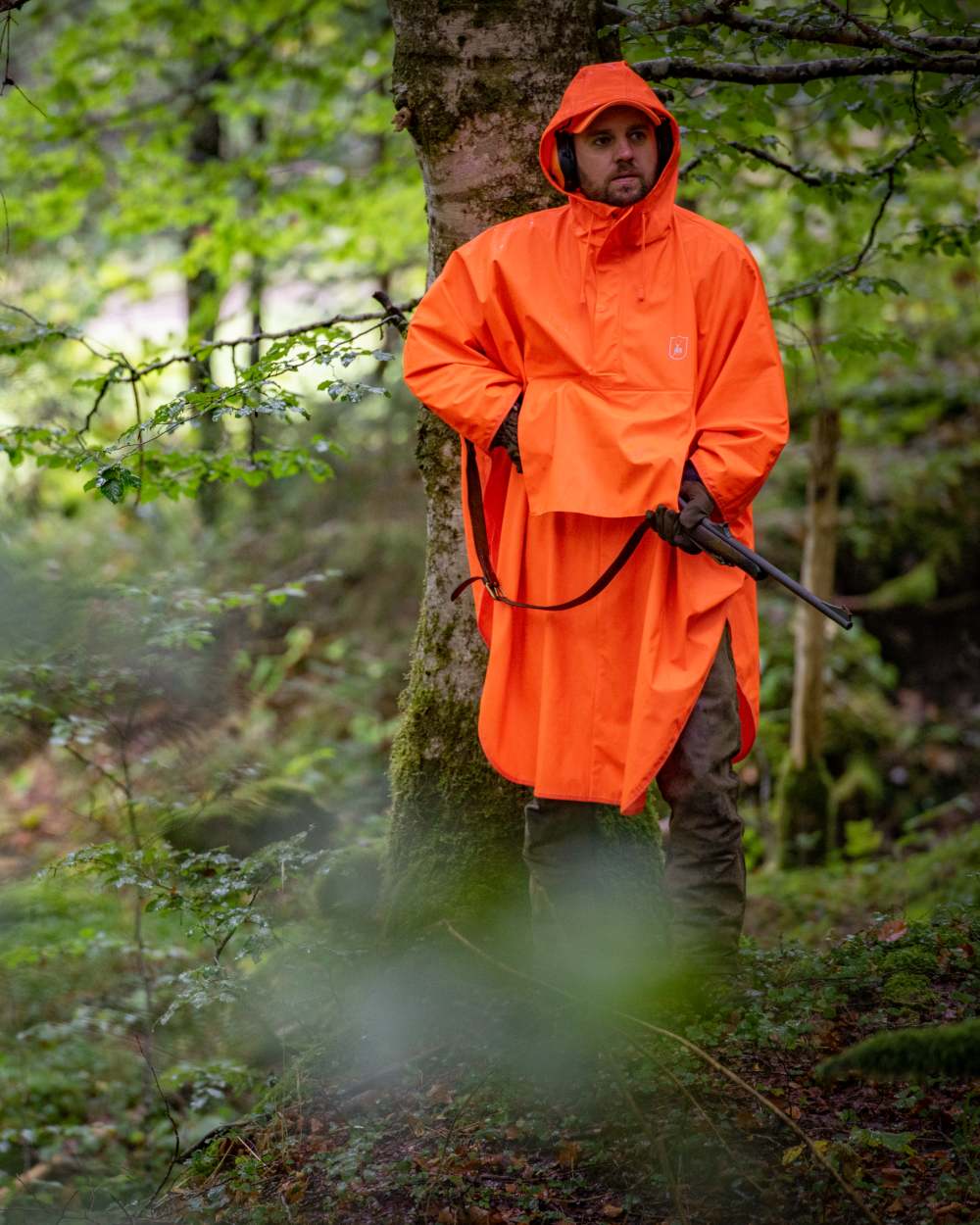 Orange coloured Deerhunter Hurricane Rain Poncho on forest background #colour_orange