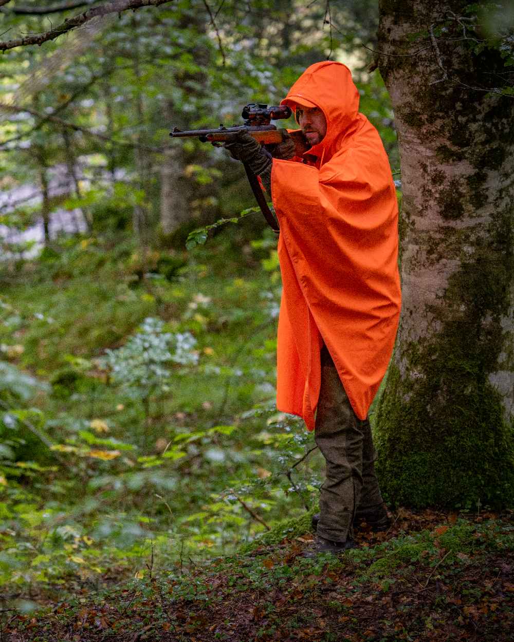 Orange coloured Deerhunter Hurricane Rain Poncho on forest background #colour_orange