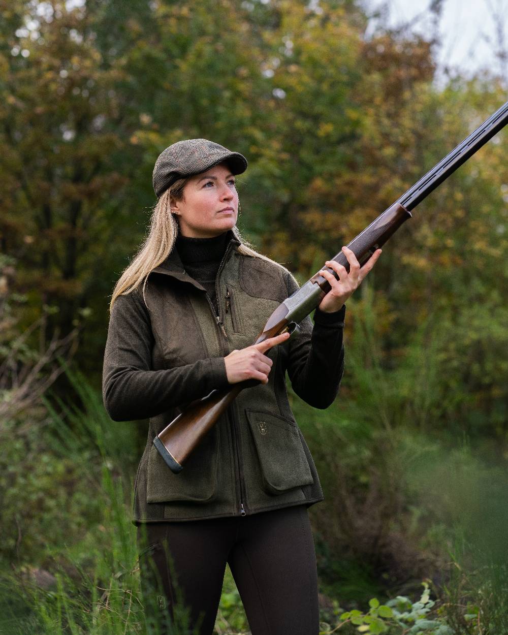 Graphite Green coloured Deerhunter Lady Pam Shooting Waistcoat on forest background #colour_graphite-green