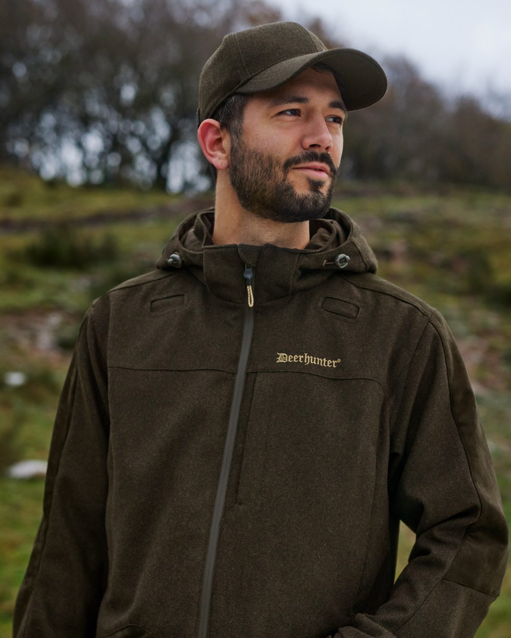 Loden Wood Coloured Deerhunter Tatra Cap With Earflaps On A Forest Background #colour_loden-wood