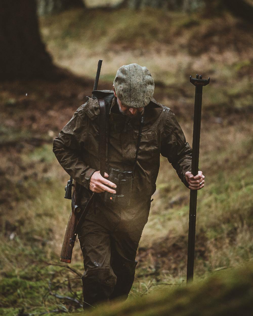 Canteen coloured Deerhunter Track Rain Trousers on forest background #colour_canteen