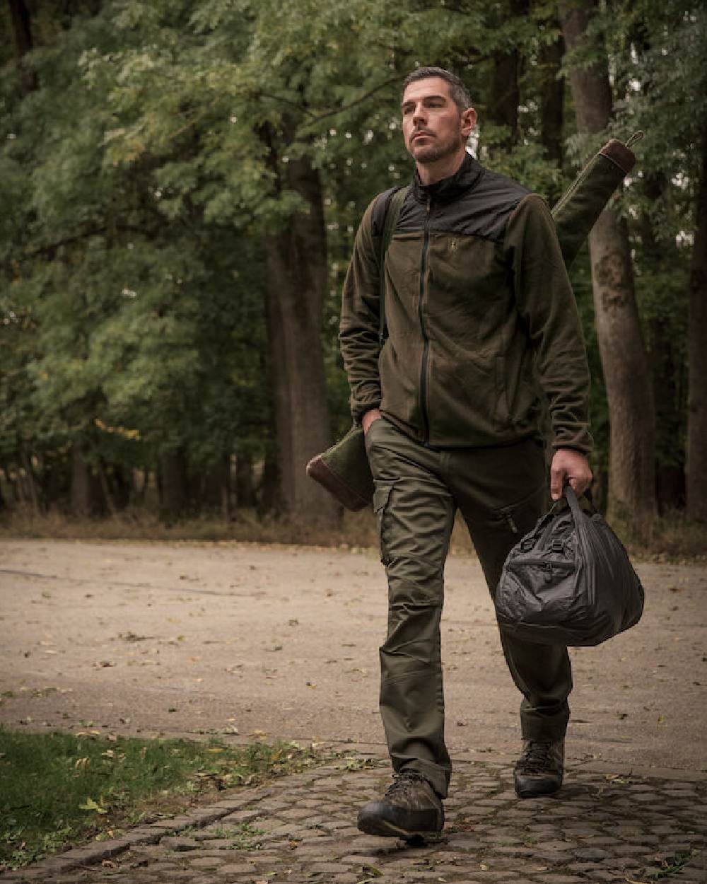 Rifle Green coloured Deerhunter Traveler Trousers on forest background #colour_rifle-green