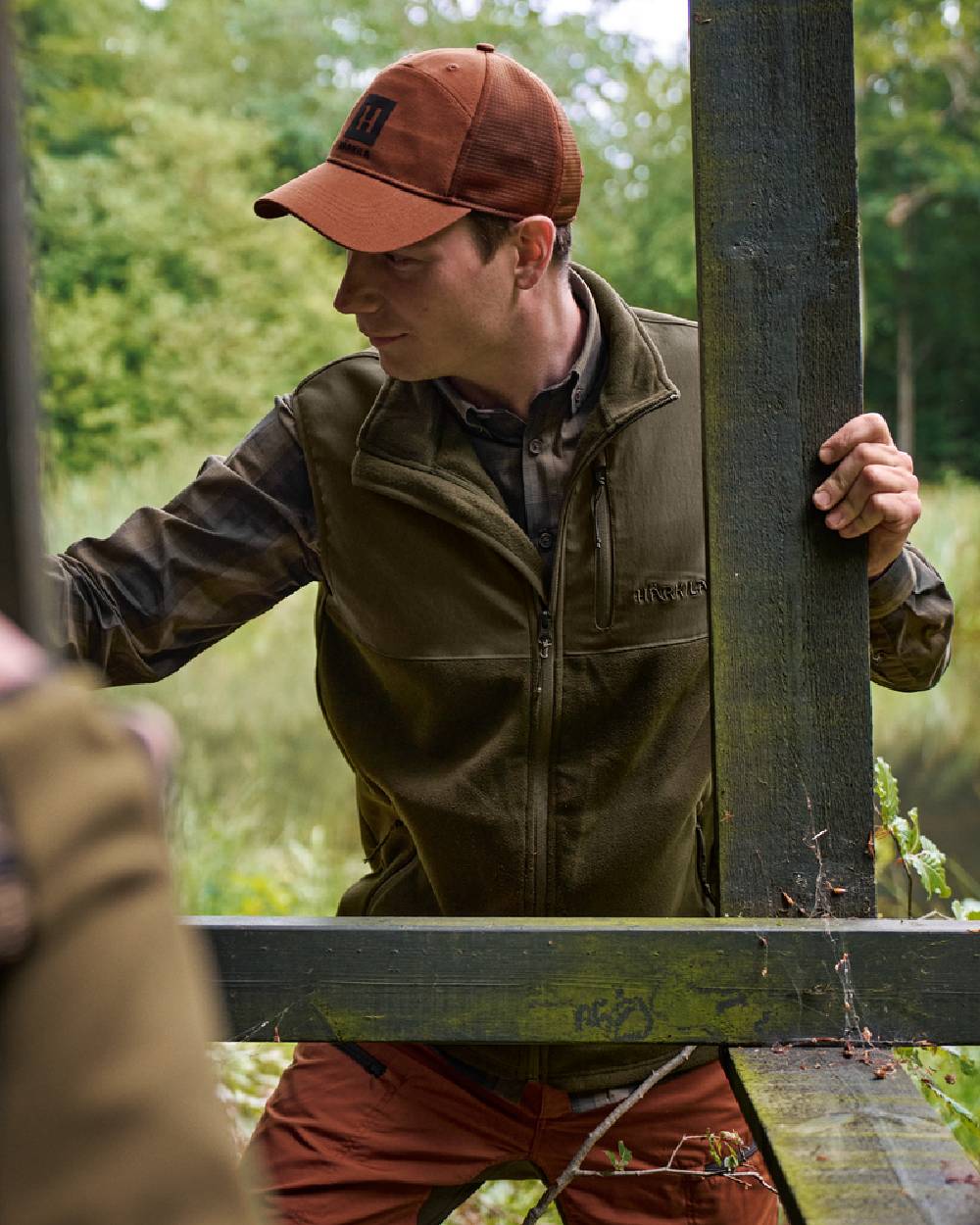 Hunting Green Willow Green Coloured Harkila Fjell Fleece Waistcoat on forest background #colour_hunting-green-willow-green