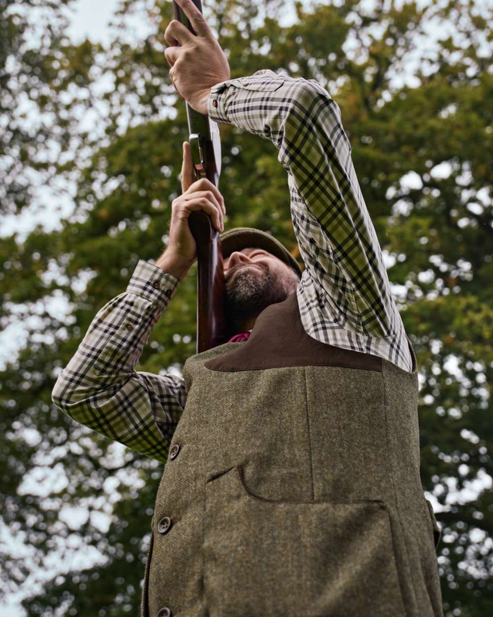 Forest Green Herringbone coloured Harkila Kenmore Shooting Waistcoat on forest background #colour_forest-green-herringbone