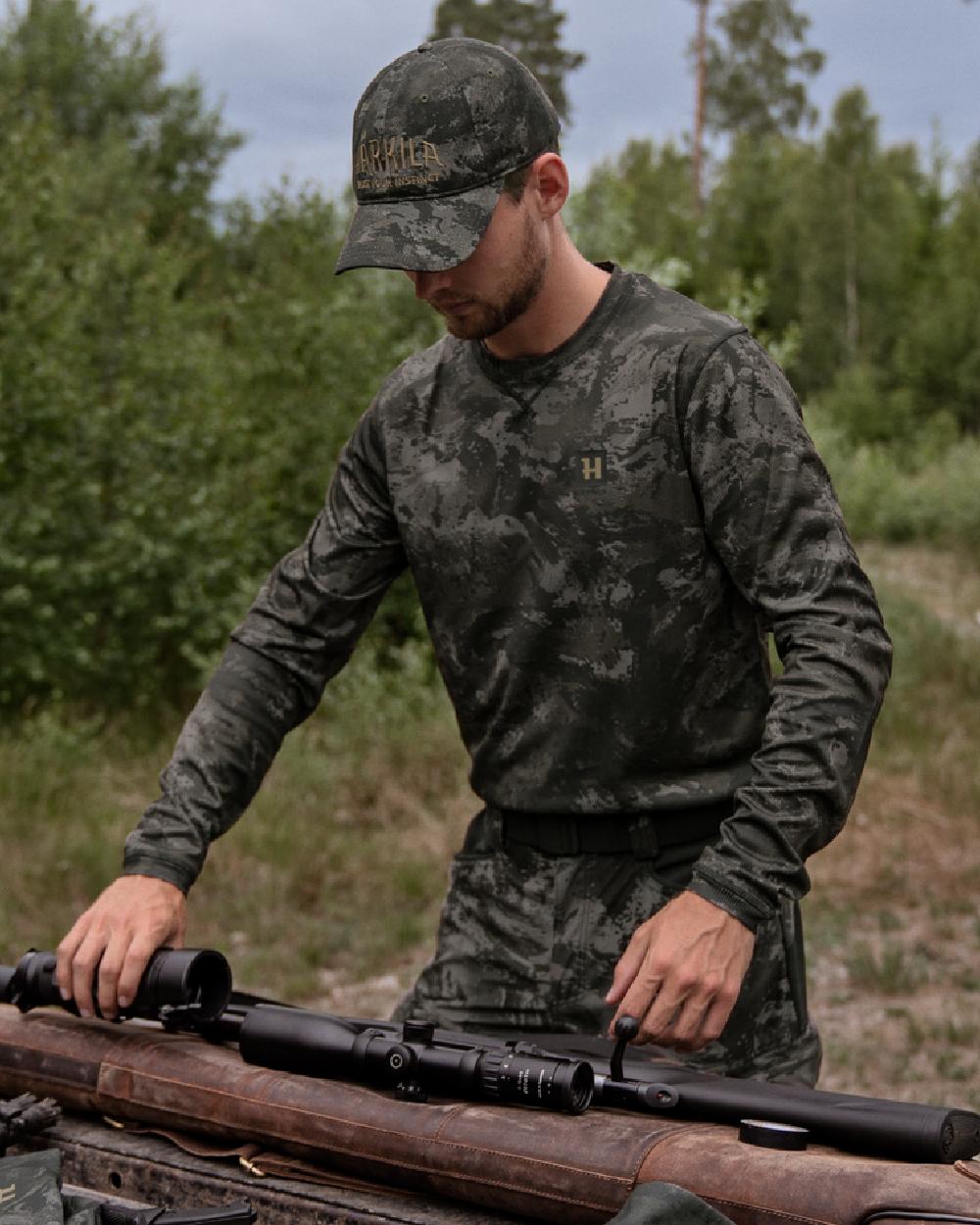 AXIS Black Coloured Harkila NOCTYX Camo Long Sleeve T-Shirt on forest background #colour_axis-black