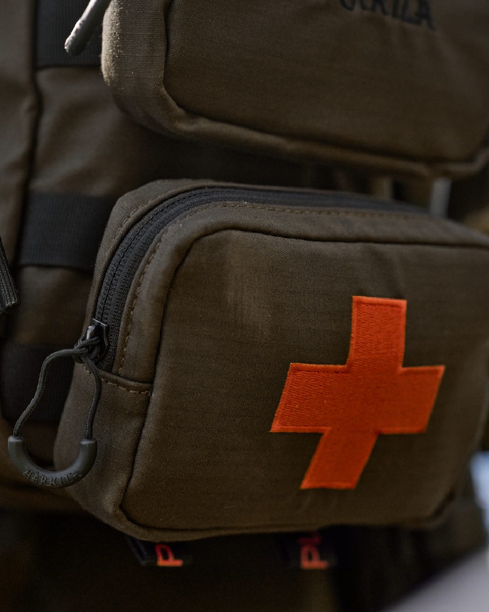 Willow Green Coloured Harkila Ragnar First Aid Backpack on blurry background #colour_willow-green