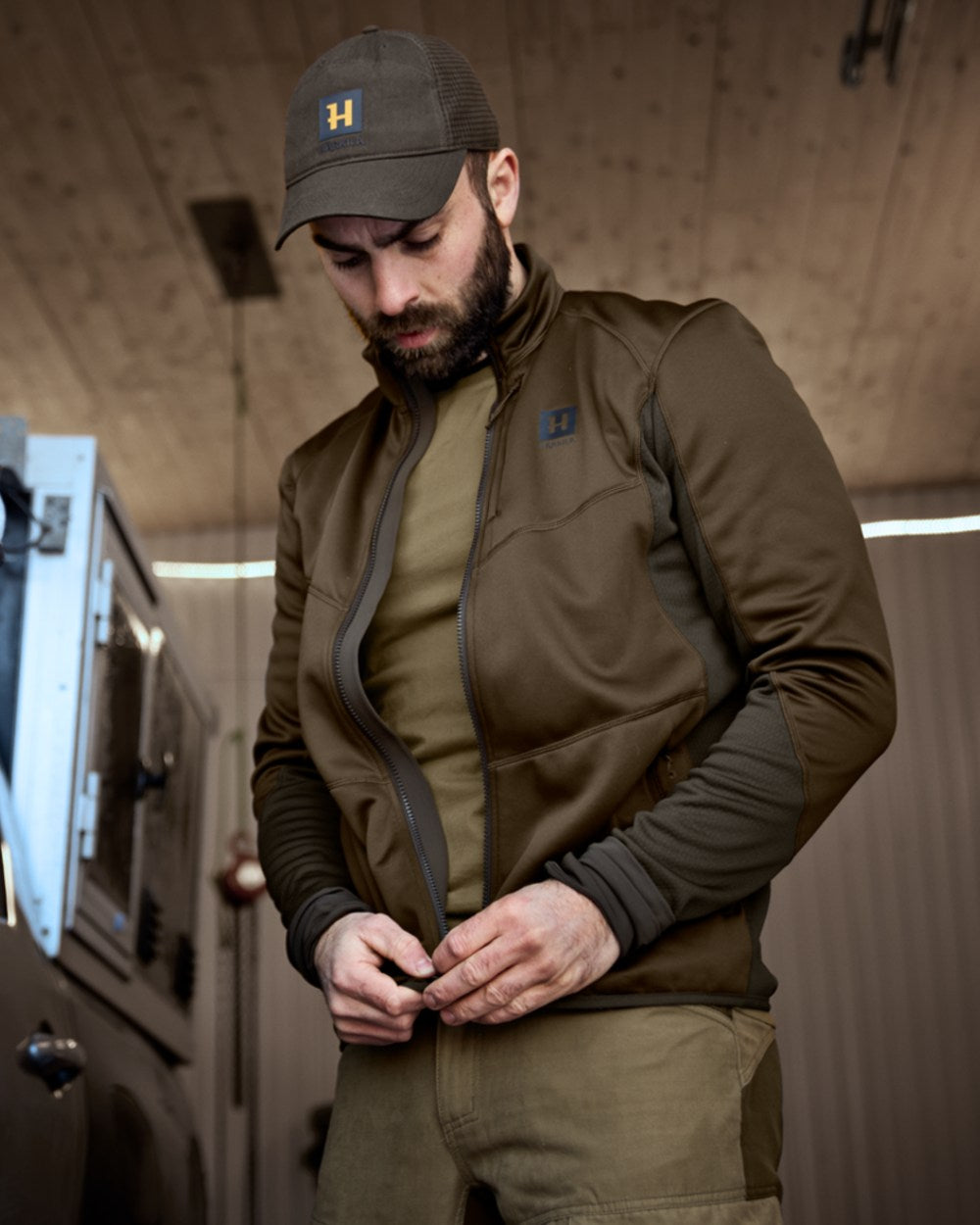 Willow Green Deep Brown Coloured Harkila Scandinavian Fleece Jacket on house background #colour_willow-green-deep-brown
