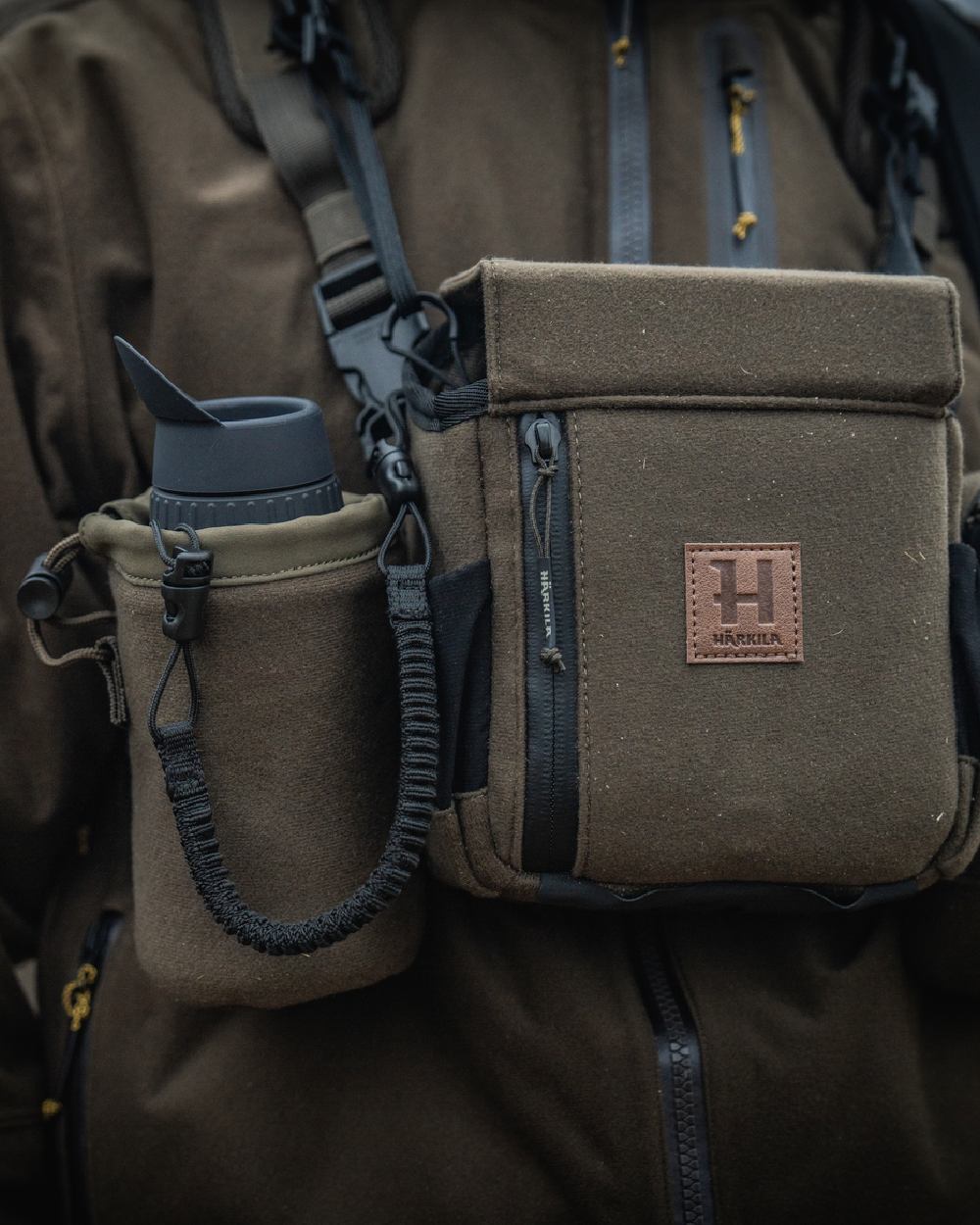 Dark Willow Green Coloured Harkila Thermal Spotter Pouch on blurry background #colour_dark-willow-green