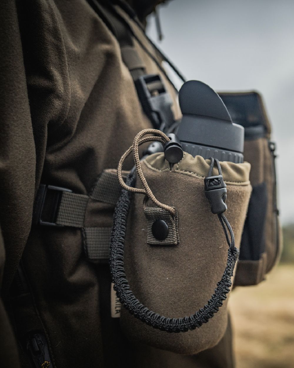 Dark Willow Green Coloured Harkila Thermal Spotter Pouch on blurry background #colour_dark-willow-green
