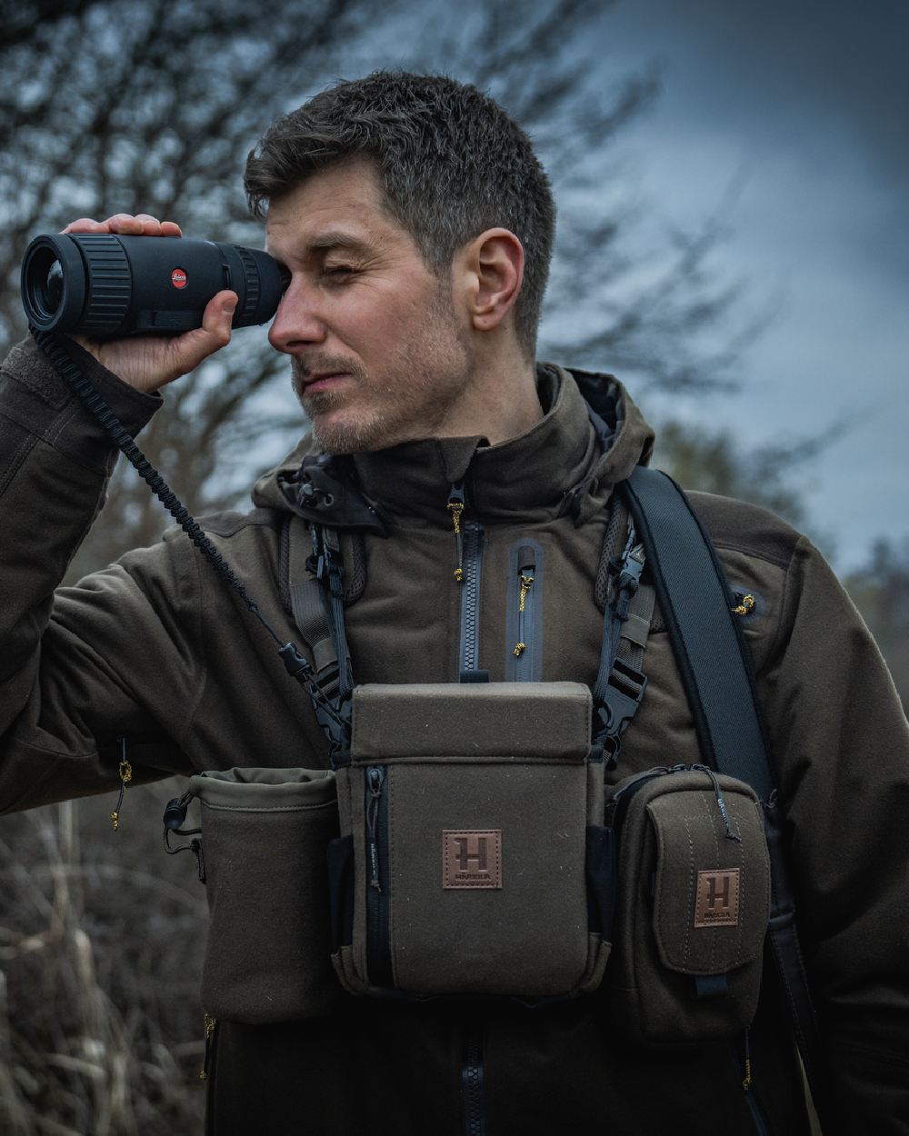 Dark Willow Green Coloured Harkila Thermal Spotter Pouch on blurry background #colour_dark-willow-green