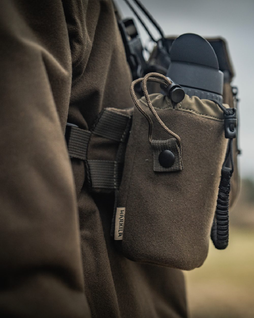 Dark Willow Green Coloured Harkila Thermal Spotter Pouch on blurry background #colour_dark-willow-green