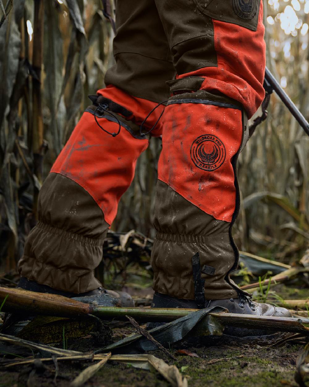 Orange Blaze Willow Green Coloured Harkila Wildboar Pro Gaiters on farm background #colour_orange-blaze-willow-green