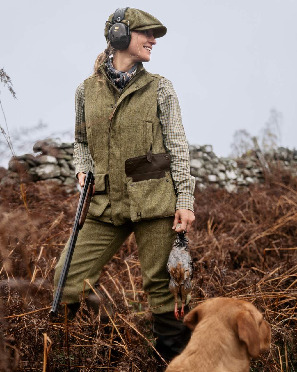 Olive Coloured Harkila Womens Jura Waistcoat on forest background #colour_olive