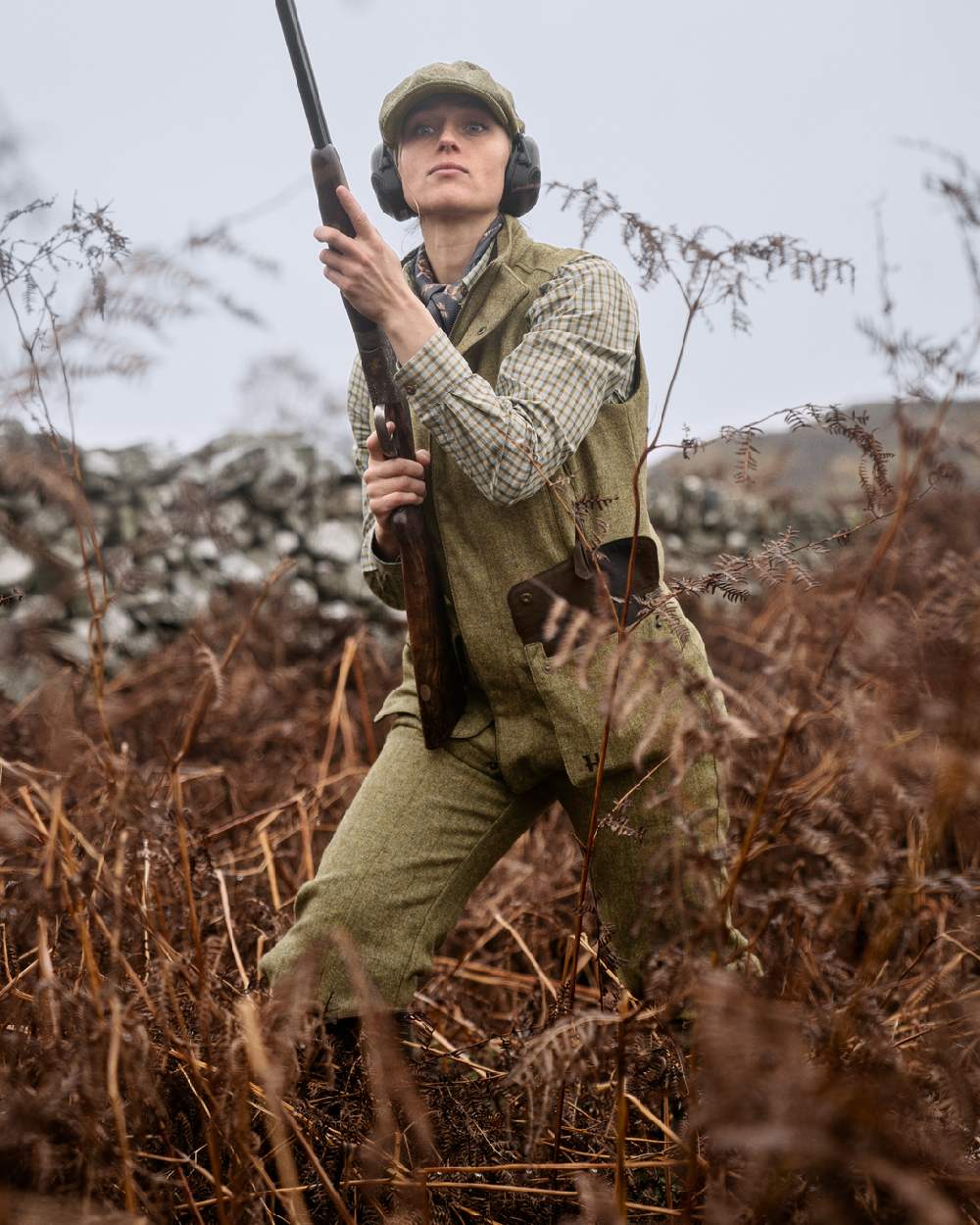 Olive Coloured Harkila Womens Jura Waistcoat on forest background #colour_olive