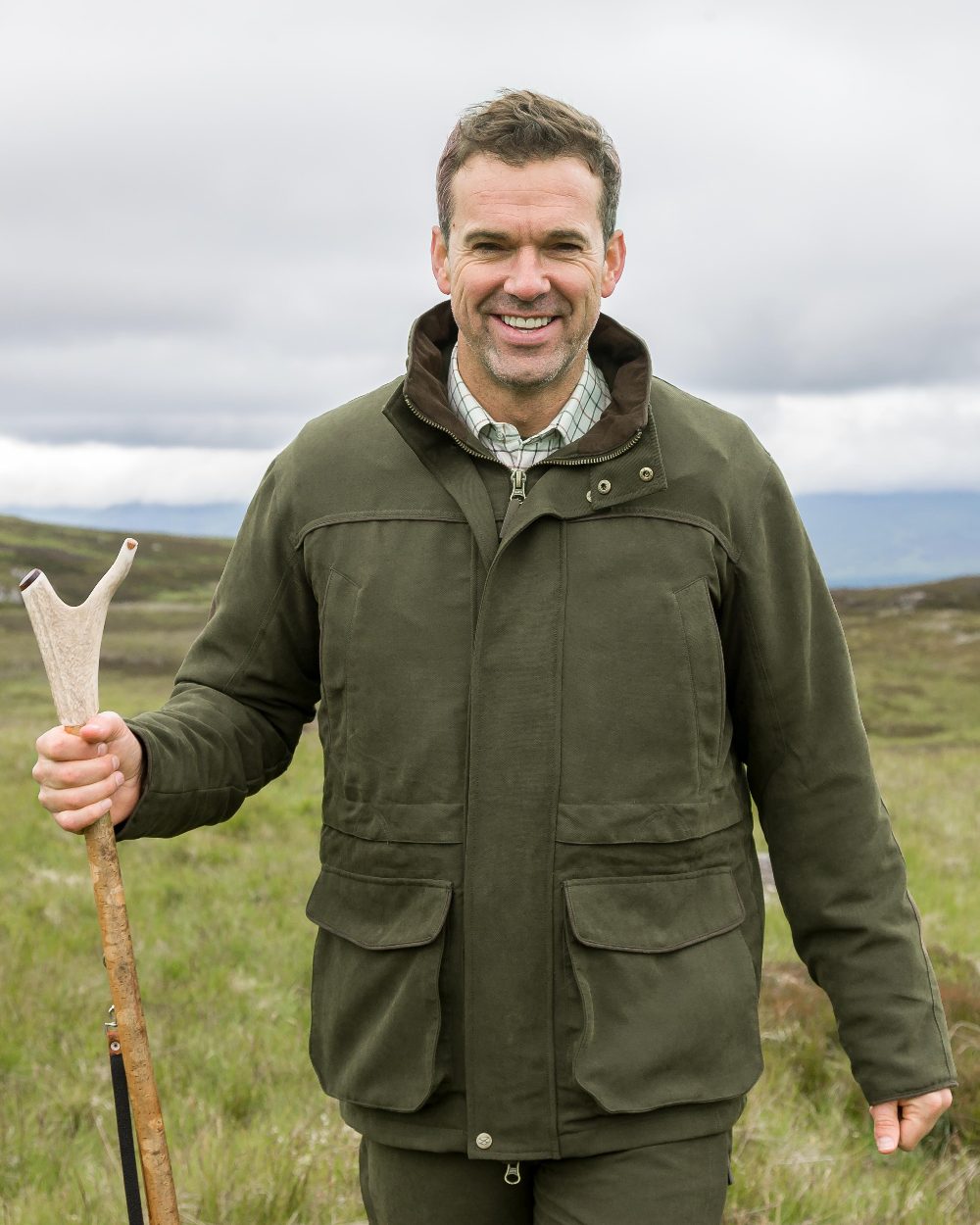 Olive Green Coloured Hoggs of Fife Kincraig Waterproof Field Jacket on countryside background #colour_olive-green