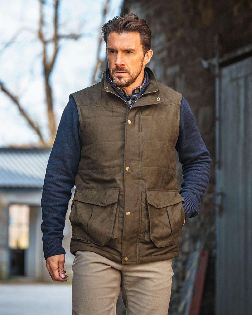 Loden coloured Hoggs of Fife Mens Glenbervie Quilted Gilet on house background #colour_loden