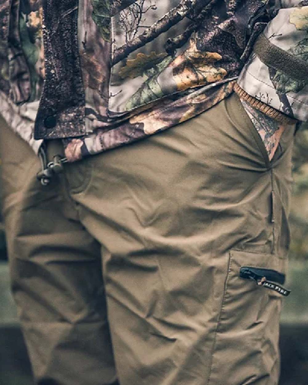 Green coloured Jack Pyke Weardale Hunting Trousers on blurry background #colour_green