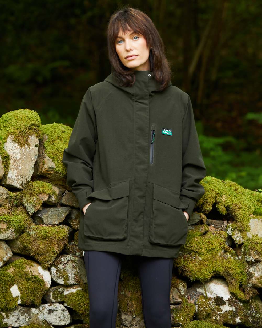 Deep Forest coloured Ridgeline Womens Rhea Jacket on stone wall background #colour_deep-forest