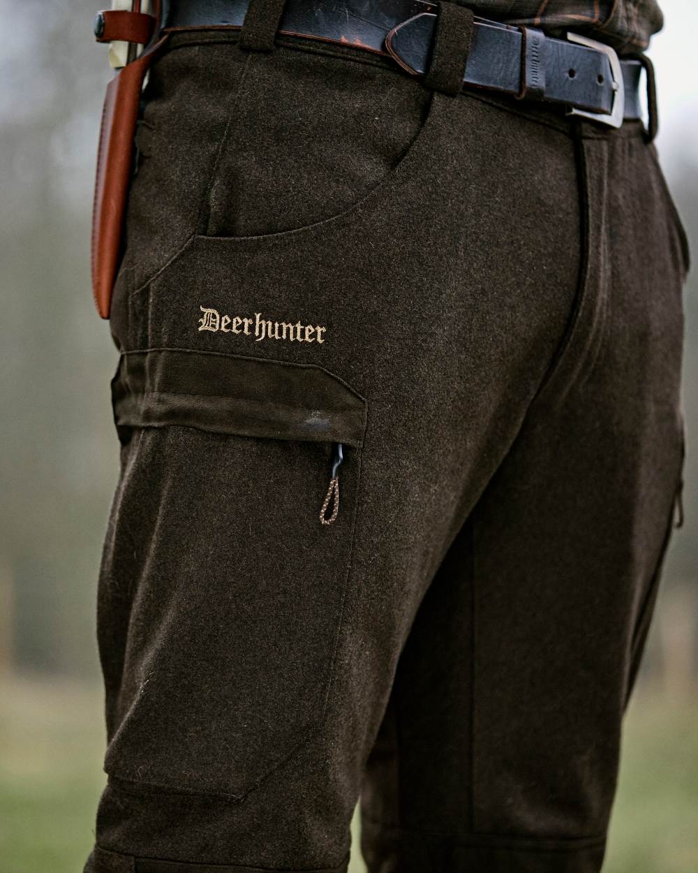 Loden Wood coloured Deerhunter Tatra Trousers on forest background #colour_loden-wood
