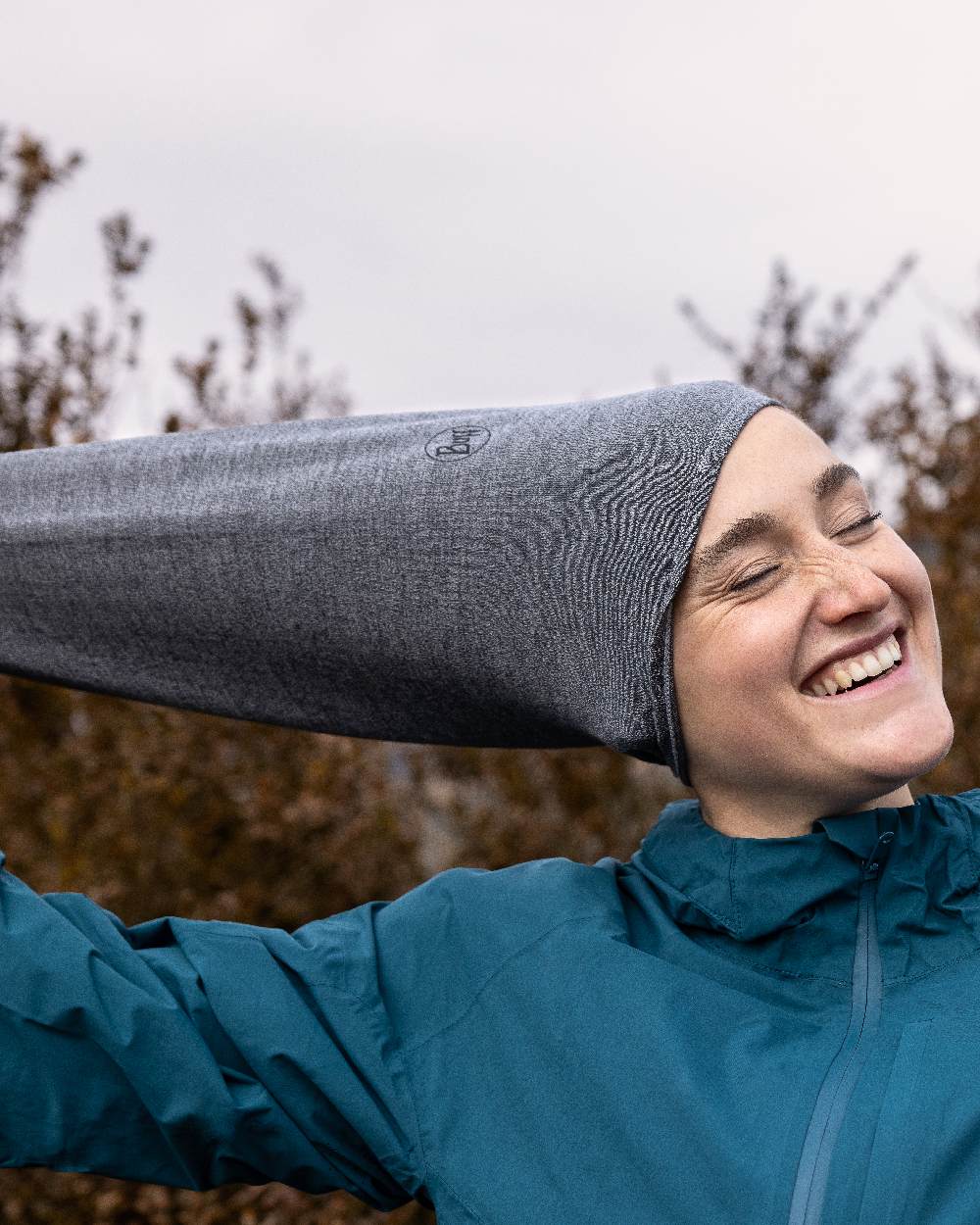 Light Grey Coloured Buff Merino Lightweight Neck Warmer on forest background #colour_light-grey