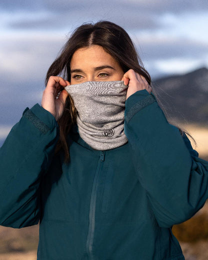 Light Grey Coloured Buff Merino Lightweight Neck Warmer on blurry background #colour_light-grey