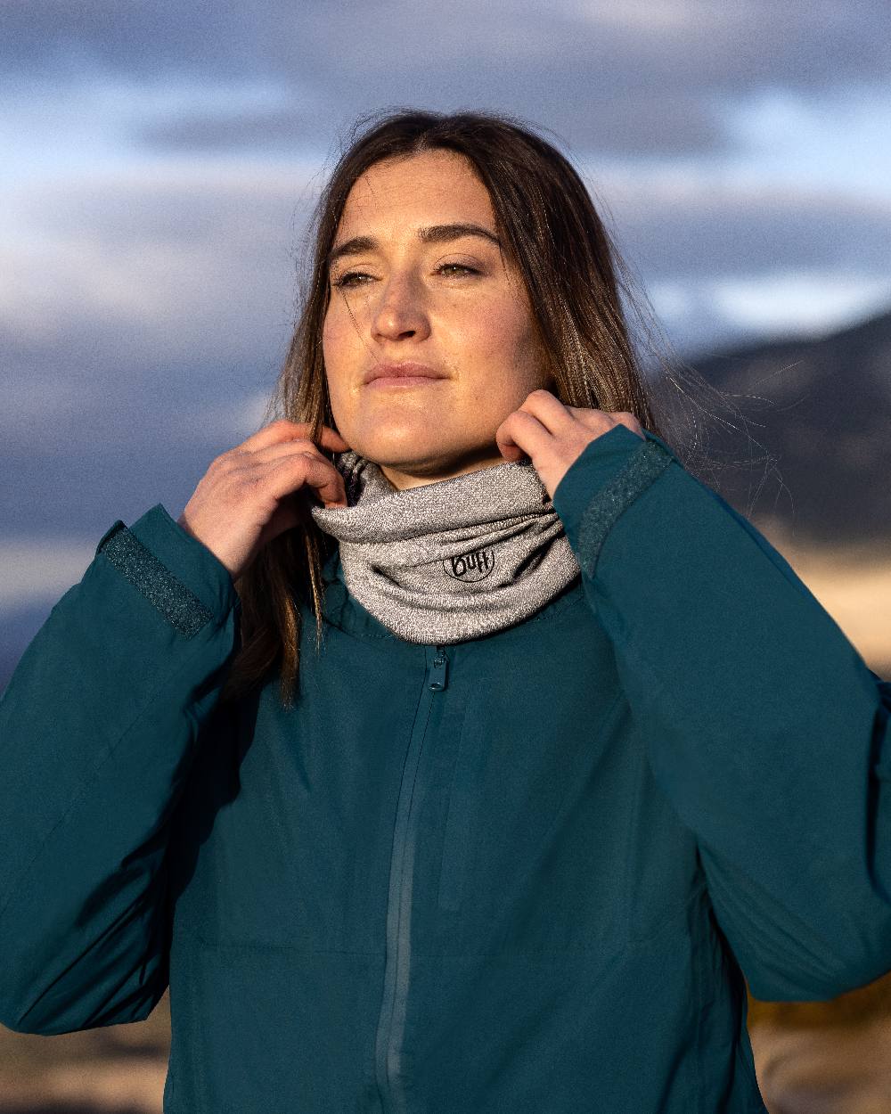 Light Grey Coloured Buff Merino Lightweight Neck Warmer on blurry background #colour_light-grey