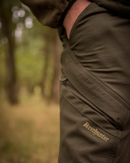 Bark Green coloured Northward Trousers on blurry background #colour_bark-green