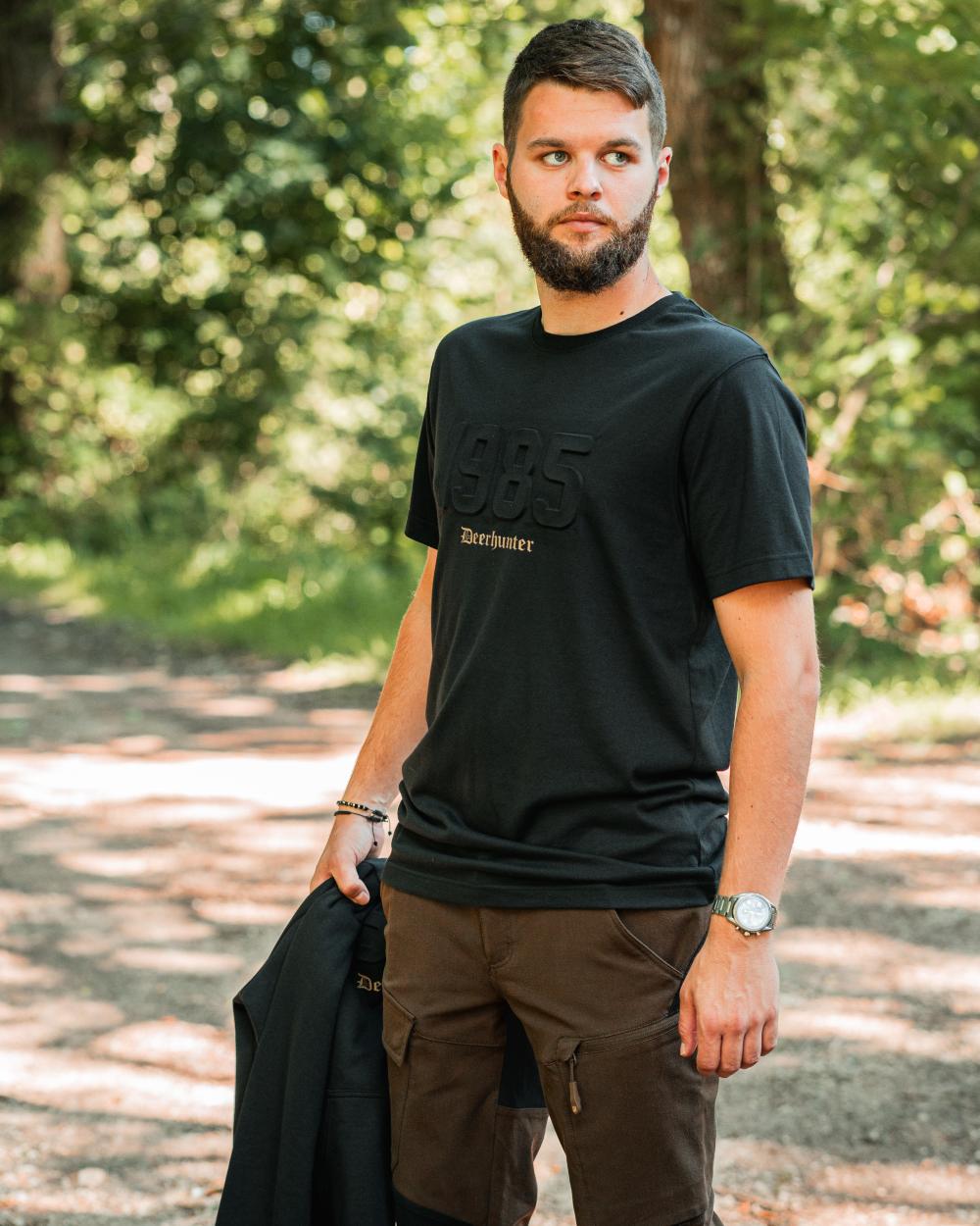 Black coloured Deerhunter Mens Jubilee T-Shirt on forest background #colour_black