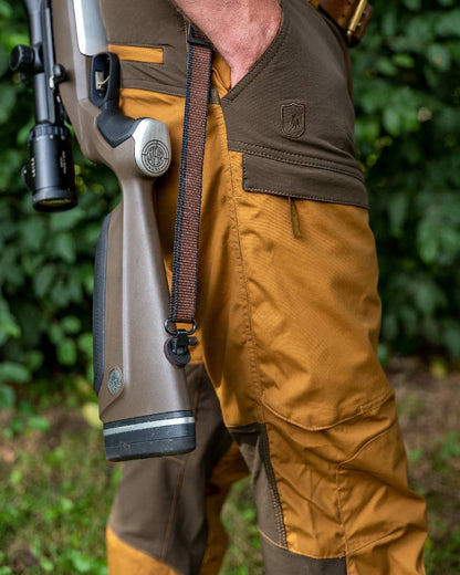 Bronze coloured Deerhunter Strike Trousers on forest background #colour_bronze
