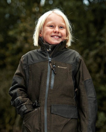 Olive Night Melange coloured Deerhunter Youth Chasse Jacket on forest background #colour_olive-night-melange
