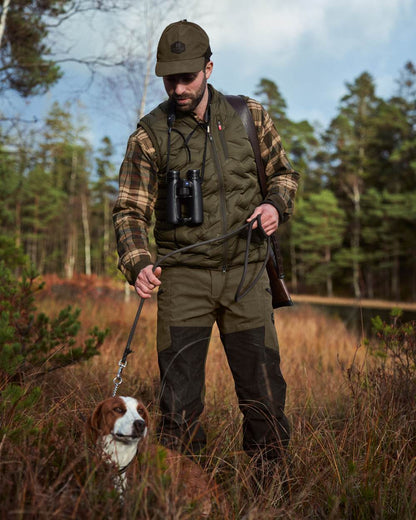 Willow Green Shadow Brown Coloured Harkila Driven Hunt HWS Leather Trousers on forest background #colour_willow-green-shadow-brown