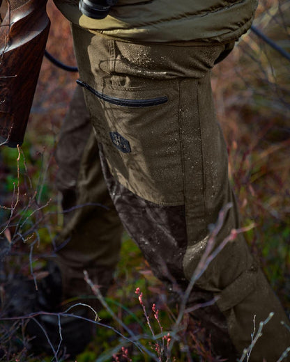 Willow Green Shadow Brown Coloured Harkila Driven Hunt HWS Leather Trousers on forest background #colour_willow-green-shadow-brown