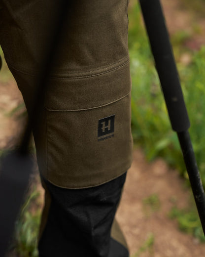 Hunting Green Coloured Harkila Finnmark HWS Trousers on blurry background #colour_hunting-green