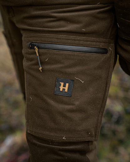 Hunting Green Shadow Brown Coloured Harkila Forest Hunter GTX Trousers on blurry background #colour_hunting-green-shadow-brown