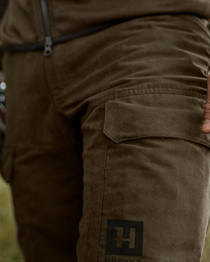 Willow Green Deep Brown Coloured Harkila Scandinavian Trousers on forest background #colour_willow-green-deep-brown