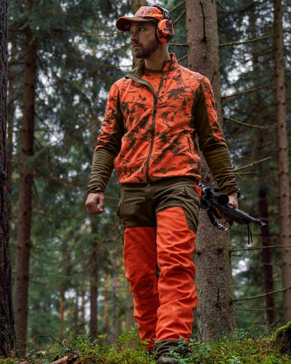 Wildboar Orange Coloured Harkila Wildboar Pro Camo Fleece Jacket on forest background #colour_wildboar-orange