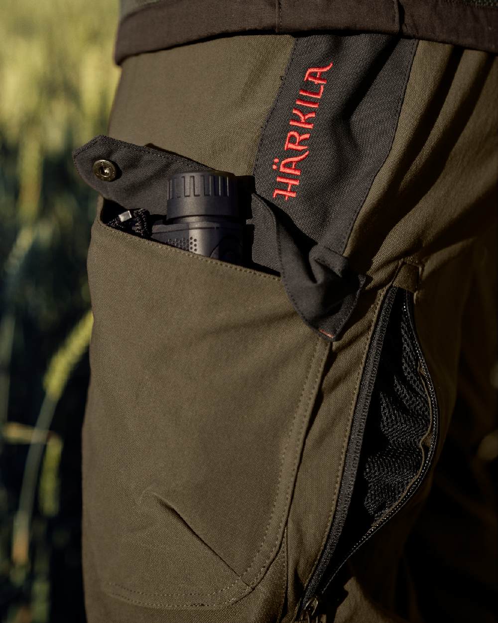 Willow Green Coloured Harkila Wildboar Pro Move Trousers on outdoor background #colour_willow-green