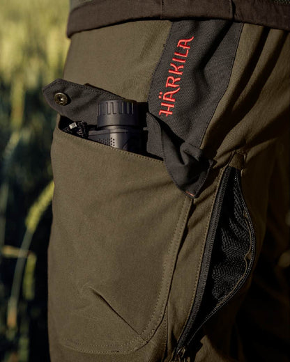 Willow Green Coloured Harkila Wildboar Pro Move Trousers on outdoor background #colour_willow-green