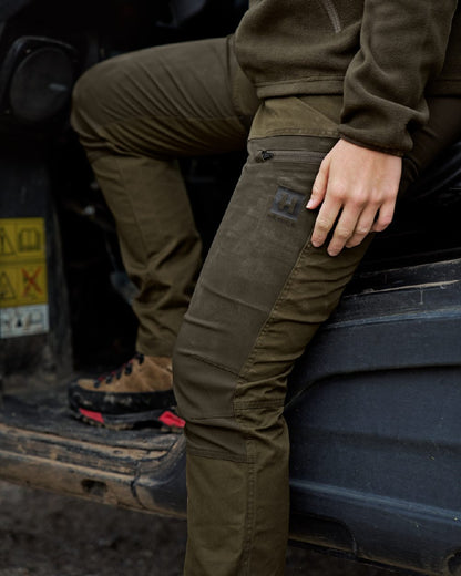 Dark Olive Willow Green Coloured Harkila Womens Fjell Trousers on tractor background #colour_dark-olive-willow-green