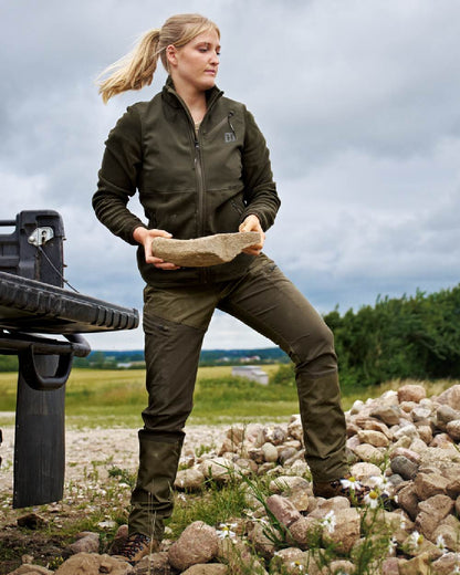 Dark Olive Willow Green Coloured Harkila Womens Fjell Trousers on countryside background #colour_dark-olive-willow-green