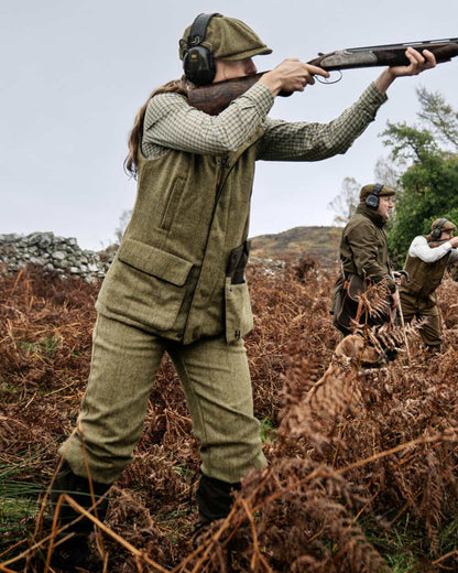 Olive Coloured Harkila Womens Jura Waistcoat on forest background #colour_olive