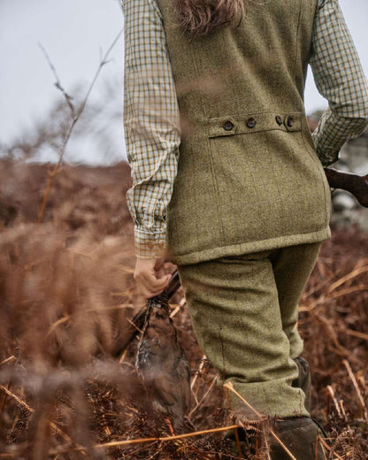 Olive Coloured Harkila Womens Jura Waistcoat on forest background #colour_olive