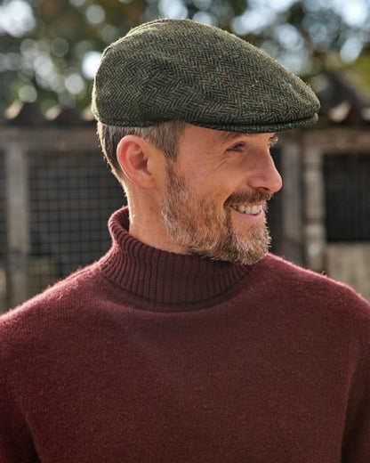 Green Coloured Hoggs of Fife Herringbone Waterproof Tweed Flat Cap on blurry background #colour_green