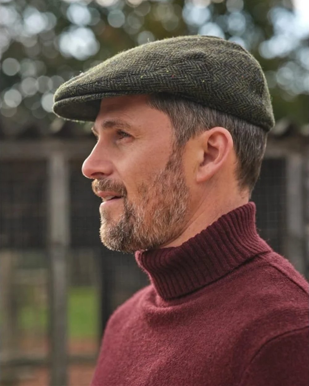 Green Coloured Hoggs of Fife Herringbone Waterproof Tweed Flat Cap on blurry background #colour_green