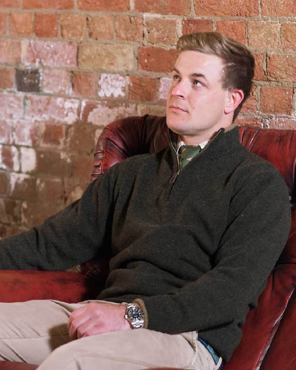 Dark Olive coloured Jack Pyke Ashcombe Lambswool Zip Knit Pullover on brick wall background #colour_dark-olive