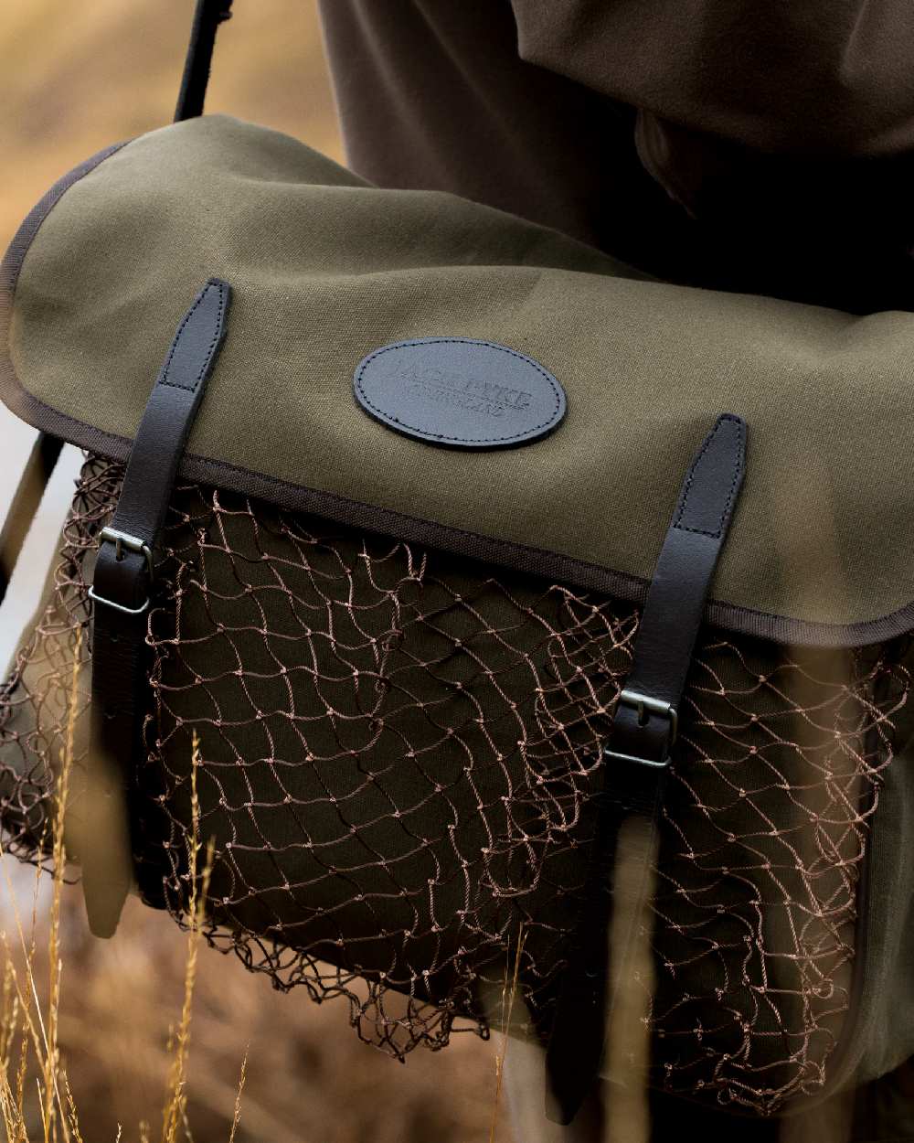 Green coloured Jack Pyke Canvas Game Bag on blurry background #colour_green