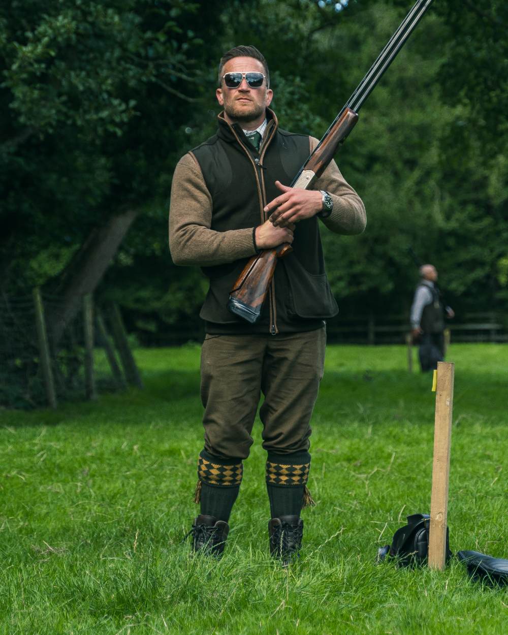 Dark Olive Jack Pyke Shooters Gilet on forest background #colour_dark-olive