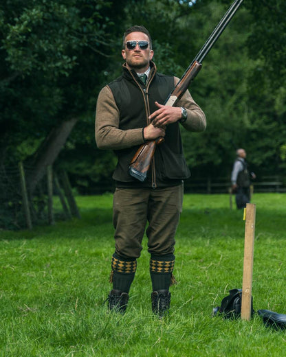 Dark Olive Jack Pyke Shooters Gilet on forest background #colour_dark-olive