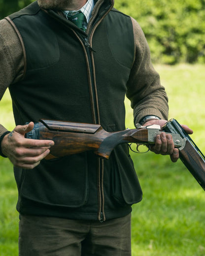 Dark Olive Jack Pyke Shooters Gilet on forest background #colour_dark-olive
